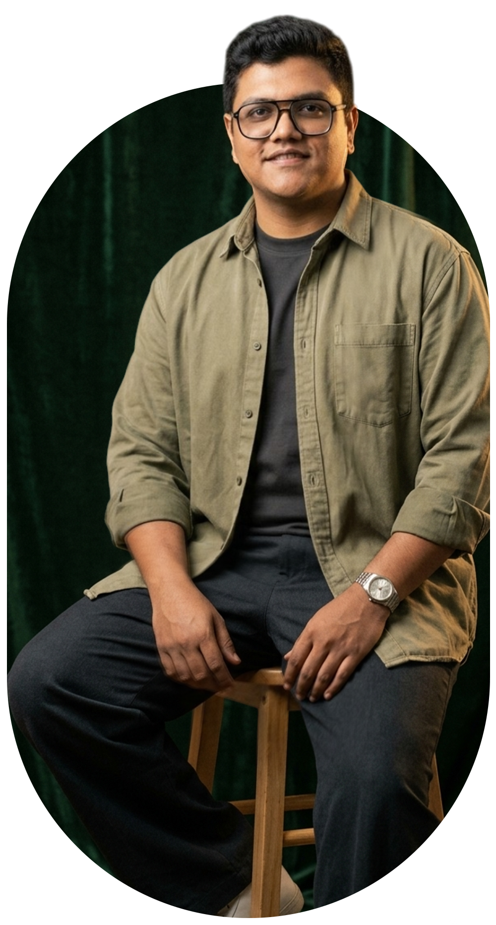Nirjhar Khan, graphic designer and art director, seated in glasses and an olive overshirt against a dark green backdrop